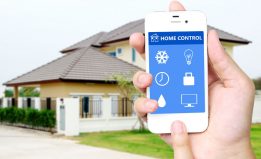 smart home hand holding white mobile smart phone with smart home application on the screen over blurred house background, smart home concept
